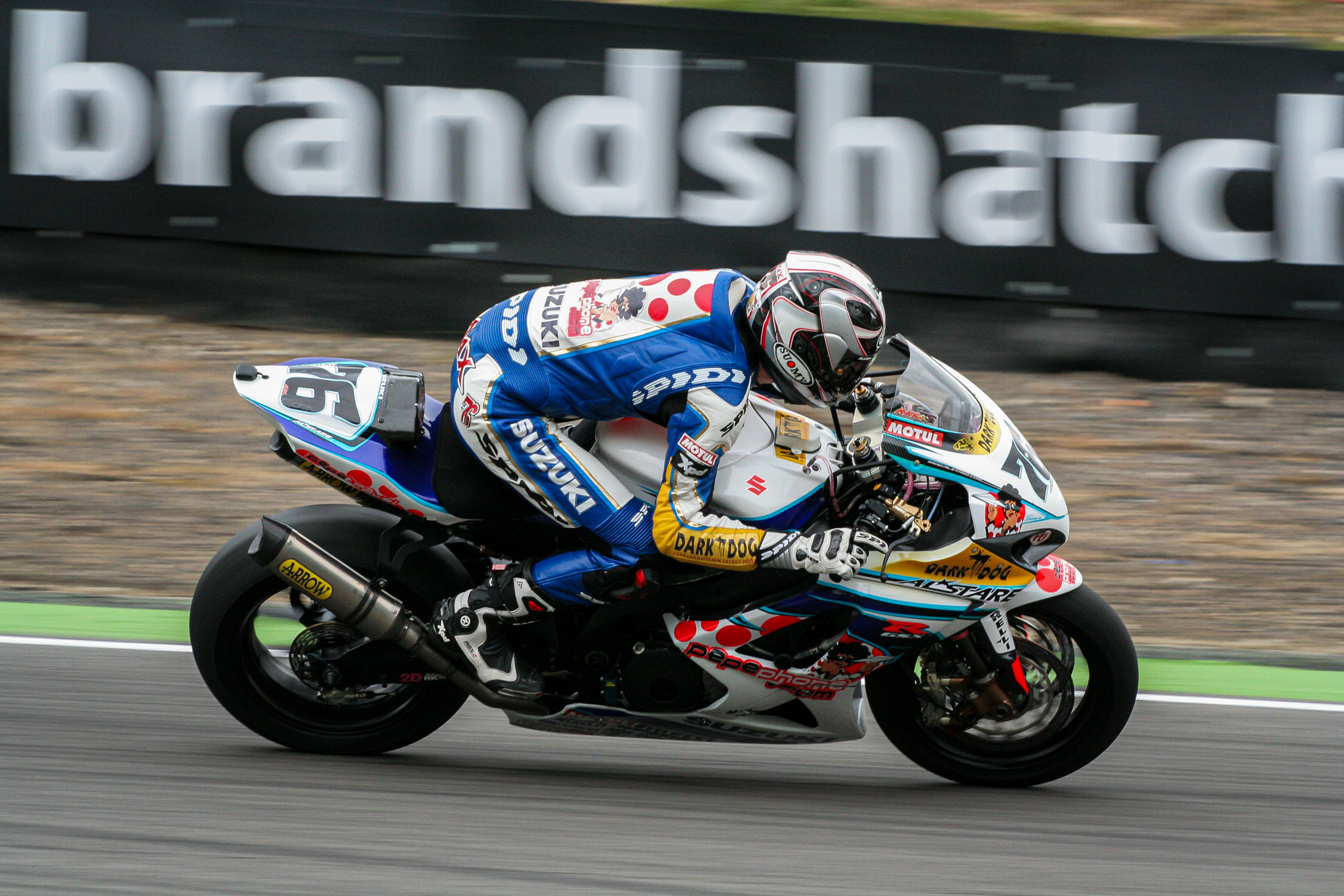 A rider leaning hard through a corner at Brands Hatch, the pit wall lettering blurred behind them